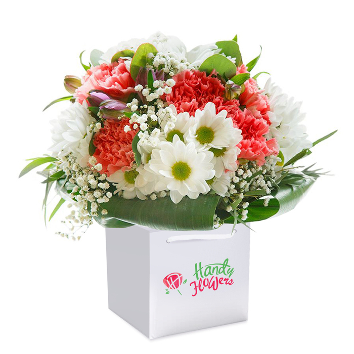At the heart of Temple, where history and quiet gardens meet lively city life, this floral arrangement radiates the essence of a fresh, premium bouquet designed by knowledgeable local hands. Vibrant coral and gentle peach carnations with distinctive ruffled petals unfold in soft clusters, their energy balanced by the brilliant white of classic daisies. Each daisy is centered with a vivid green-gold core, inviting a layer of cheerfulness reminiscent of mornings in Temple's serene green spaces. Whisper-light sprigs of baby's breath are scattered among the blooms, adding a cloud-like delicacy and softening the overall structure. Subtly woven through the left side of the bouquet are unopened buds, tinged with hints of purple and pink, which offer depth and an appealing sense of anticipation-much like discovering a secluded bench on Victoria Embankment Gardens. Enveloping the arrangement is an abundant array of deep, glossy leaves, which not only support the bouquet's full, rounded shape but also highlight the meticulous artistry behind its creation. Securely cradled in a pristine white square gift bag with robust white ribbon handles, the arrangement is staged on a pure white background, allowing every hue and texture to emerge vibrantly. The fresh, thoughtfully layered composition is ideal for any special celebration, from birthdays to anniversaries, for anyone in Temple wishing to convey affection or mark a meaningful moment with natural beauty and local character.